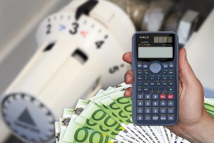 Kalkulator in evrski bankovci v roki, v ozadju radiatorski termostat.