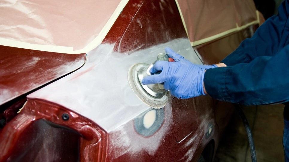 Avtomehanik polira karoserijo rdečega avtomobila.