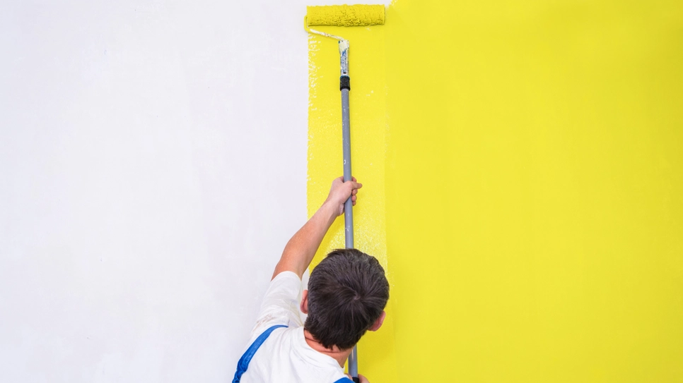 slikopleskar nanaša rumeno barvo na steno, dokončal je že polovico stene