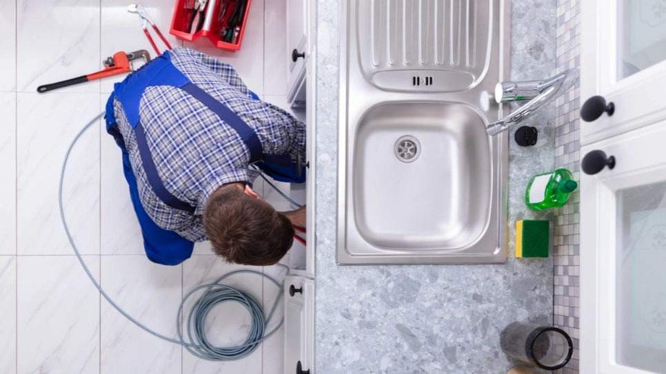 Vodovodar popravlja odtok pod umivalnikom v kuhinji. Slikano iz ptičje perspektive.