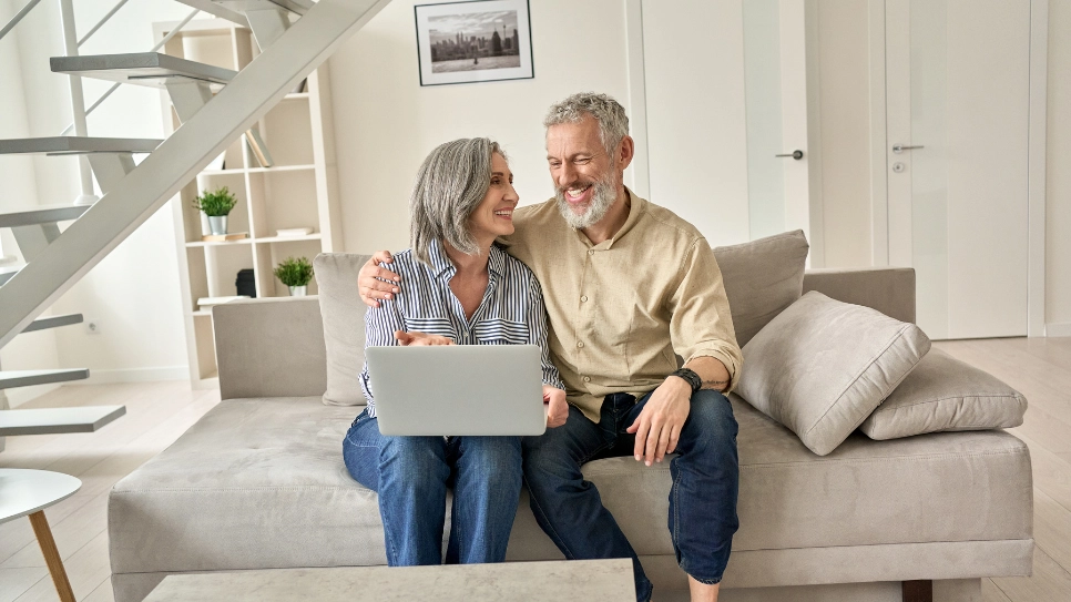 Starejši par na kavču si na računalniku ogleduje možnosti za življenjsko zavarovanje.