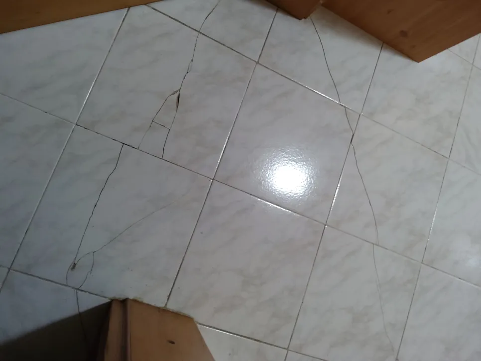 Cracked white floor tiles indicating structural issues in home flooring.