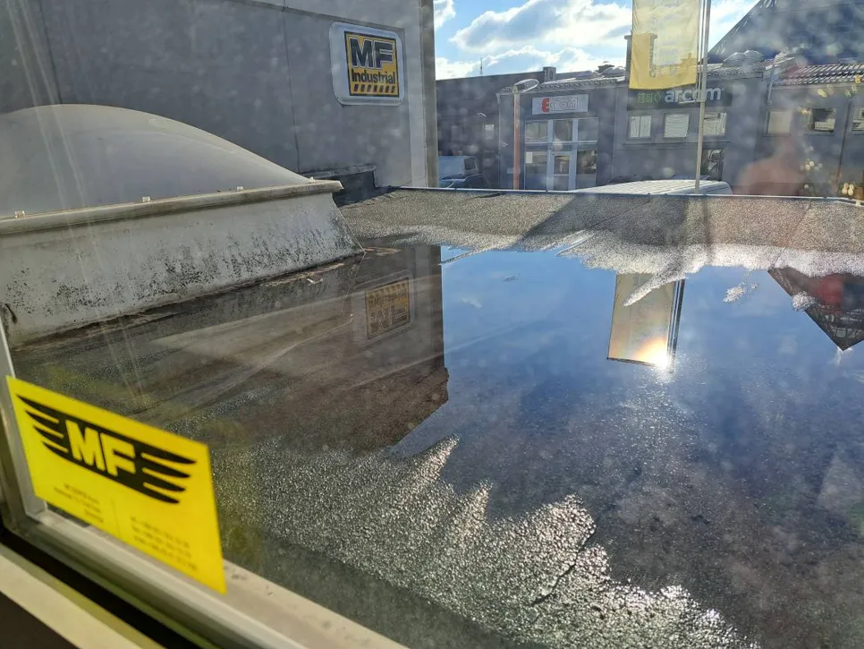 Water pooling on a flat commercial roof under sunlight, reflecting nearby buildings and sky.