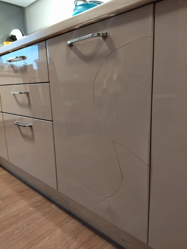 Glossy kitchen cabinet with visible cracks on the surface, showing damage in a modern kitchen setting.