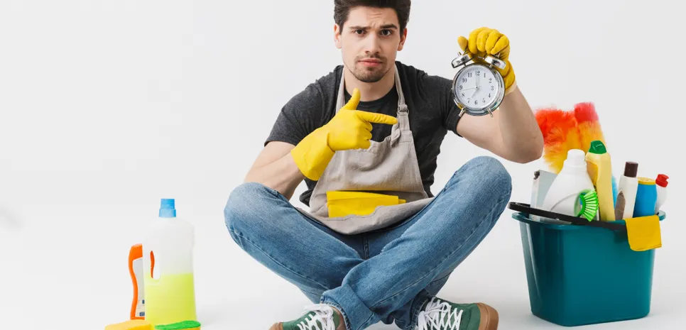 Mlad moški obkrožen s čistili kaže na budilko.