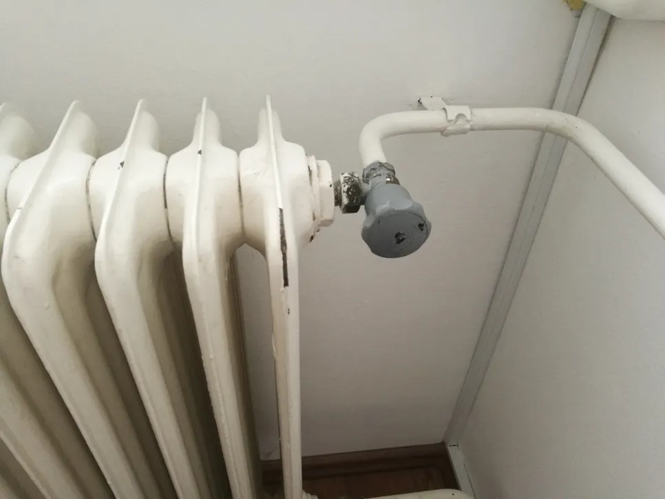 A radiator with a potentially leaking valve in a home setting, showing signs of wear.