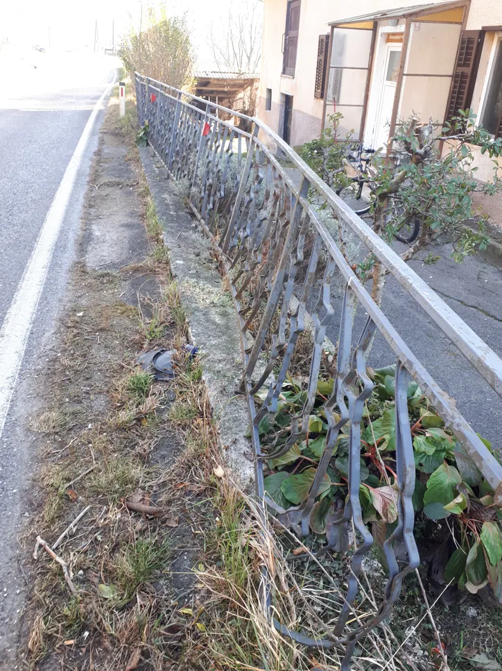 Bent metal fence alongside a rural road with nearby greenery.