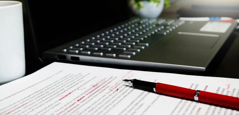 lektoriran list papirja na mizi poleg prenosnega računalnika