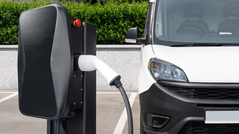 Električni kombi priklopljen na javno električno polnilnico, uporabniki pogosto preverjajo ceno polnjenja električnih avtomobilov.