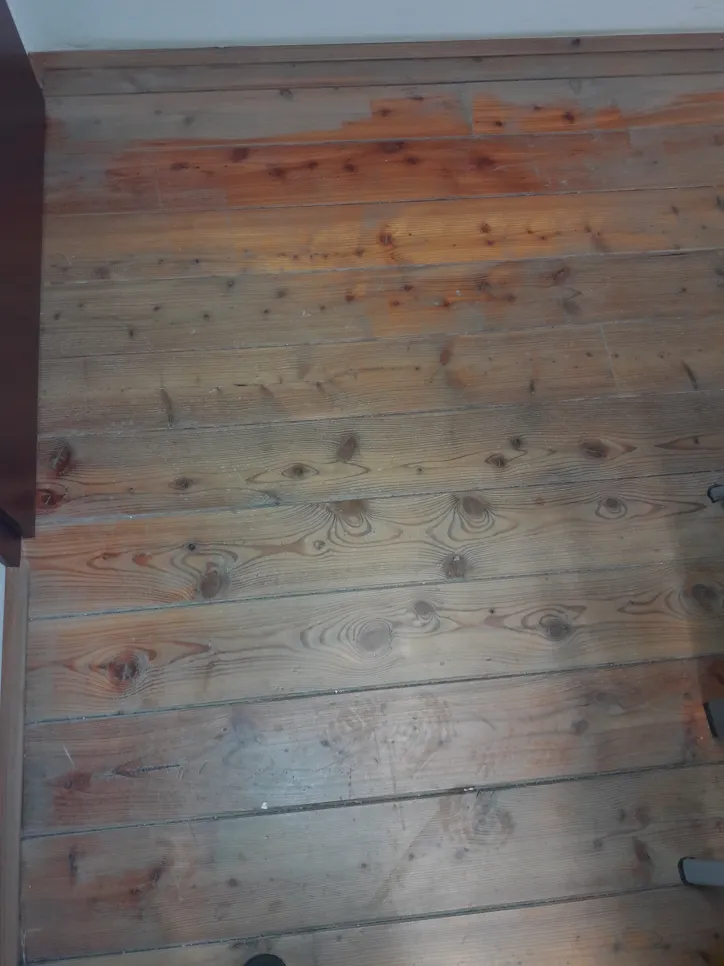Wooden floor with visible water damage and discoloration, showing darkened patches.