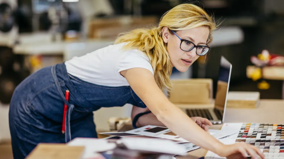 Lastnica manjšega podjetja za se sklanja nad mizo z vzorci.