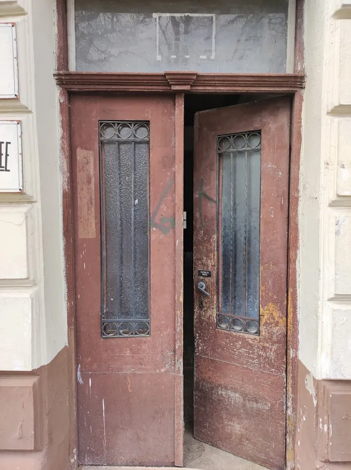 A vintage wooden door with chipped paint and decorative glass panels stands slightly open, revealing its age.