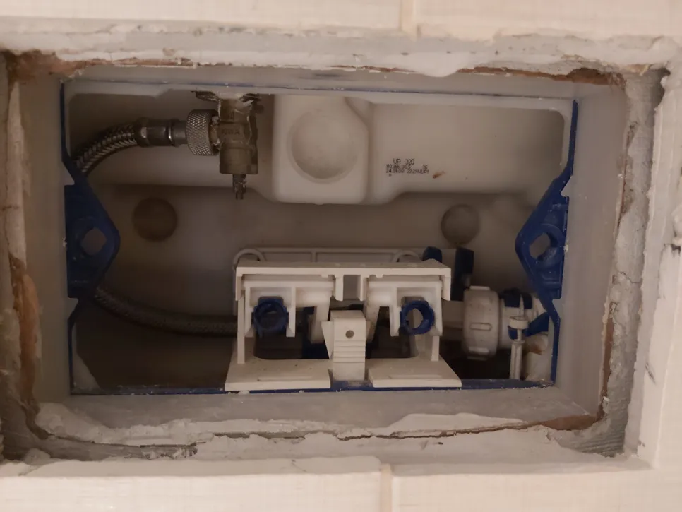Inside view of toilet cistern with exposed valve and plumbing parts, showing internal mechanism.