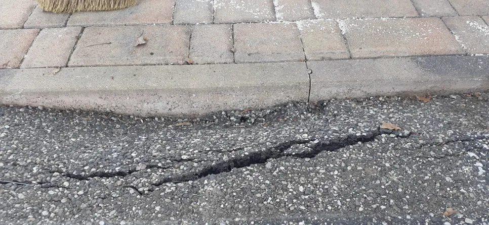 Visible crack in asphalt road next to paving stones, highlighting potential driveway issues.