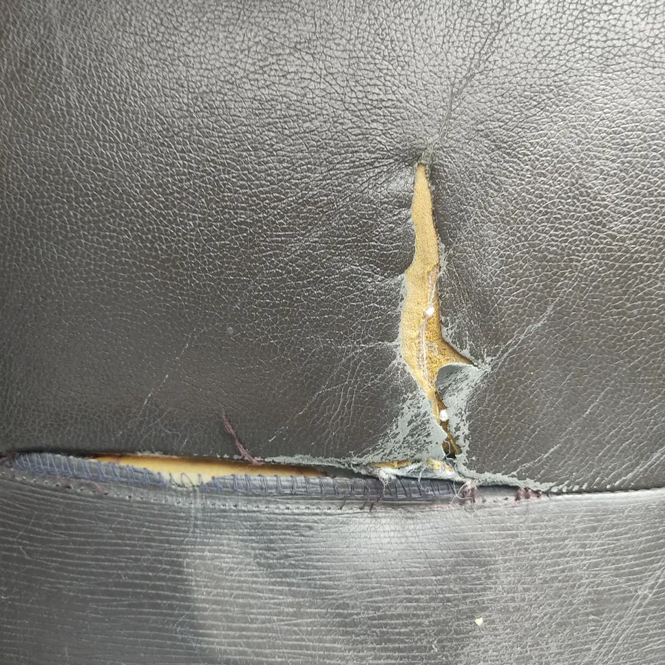 Close-up of a torn black leather car seat, revealing damaged cushioning underneath.