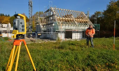 Geodetske meritve na terenu, v ozadju gradnja hiše