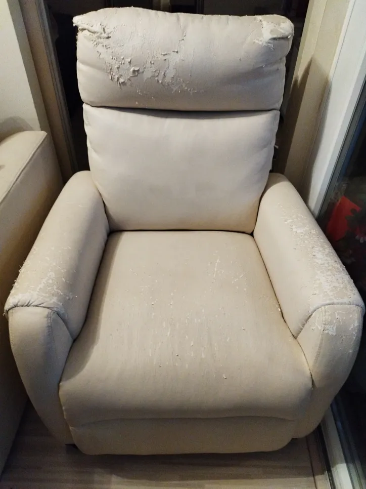 A beige leather armchair with visible wear and peeling on the headrest and armrests.