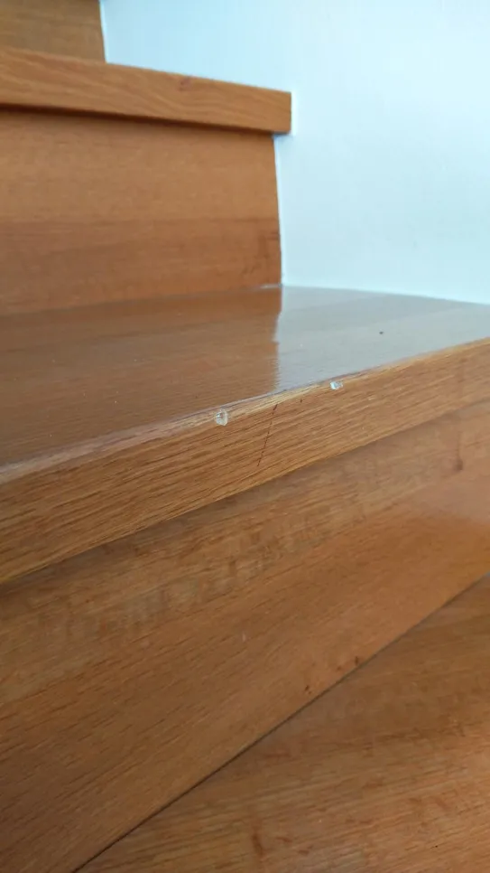 Wooden stair tread with visible scratches and dents on the surface.