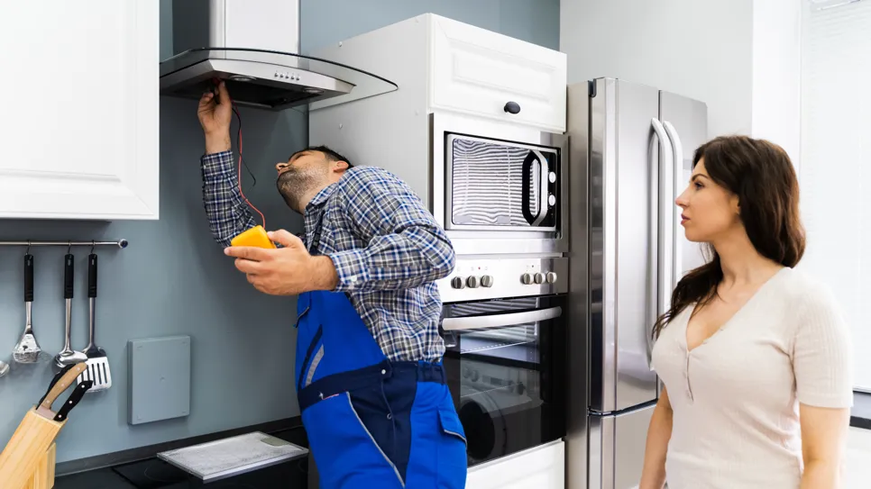 električar priključuje kuhinjsko napo na električno omrežje, medtem ko lastnica gleda