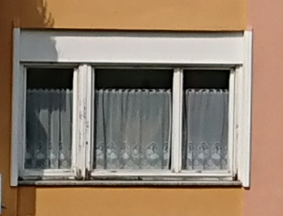 Peeling paint on an old wooden window frame against a yellow wall, indicating potential need for repair or repainting.