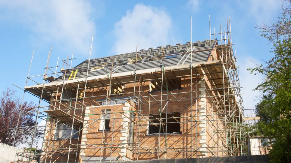 Novogradnja iz opeke v fazi prekrivanja strehe, obkrožena z gradbenimi odri