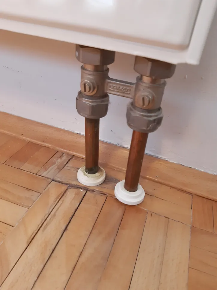 Water damage visible on wood flooring beneath radiator pipes, indicating potential leakage or spill issues.
