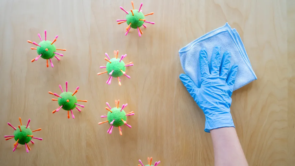 veliki zeleni mikrobi na mizi, ob njih roka s krpo