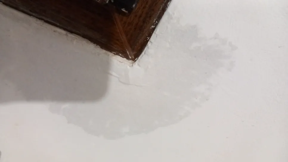 Water damage visible on a white ceiling near a corner with a dark wooden frame, indicating a potential leak.