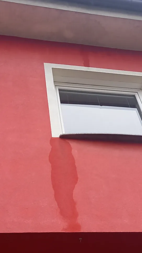 Visible water damage under window on red wall indicating potential leak issues.