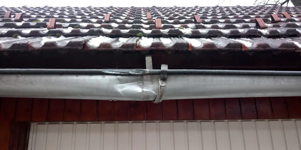 A metal rain gutter is visibly dented beneath a tiled roof, indicating possible water drainage issues.