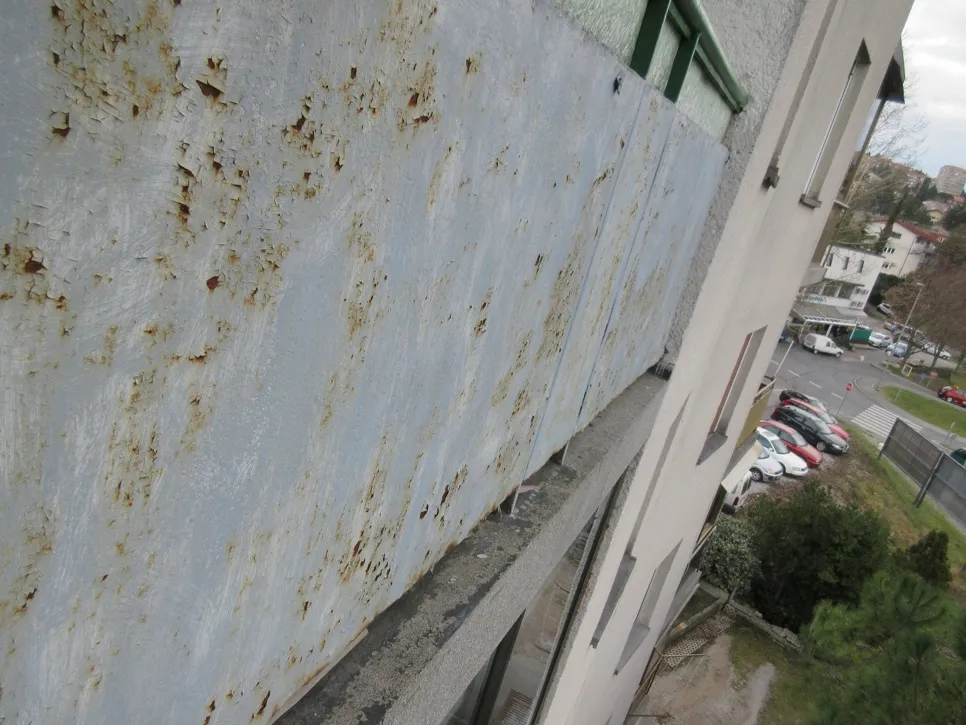 Rusty and deteriorated metal railing on an apartment balcony, showing signs of corrosion and neglect.