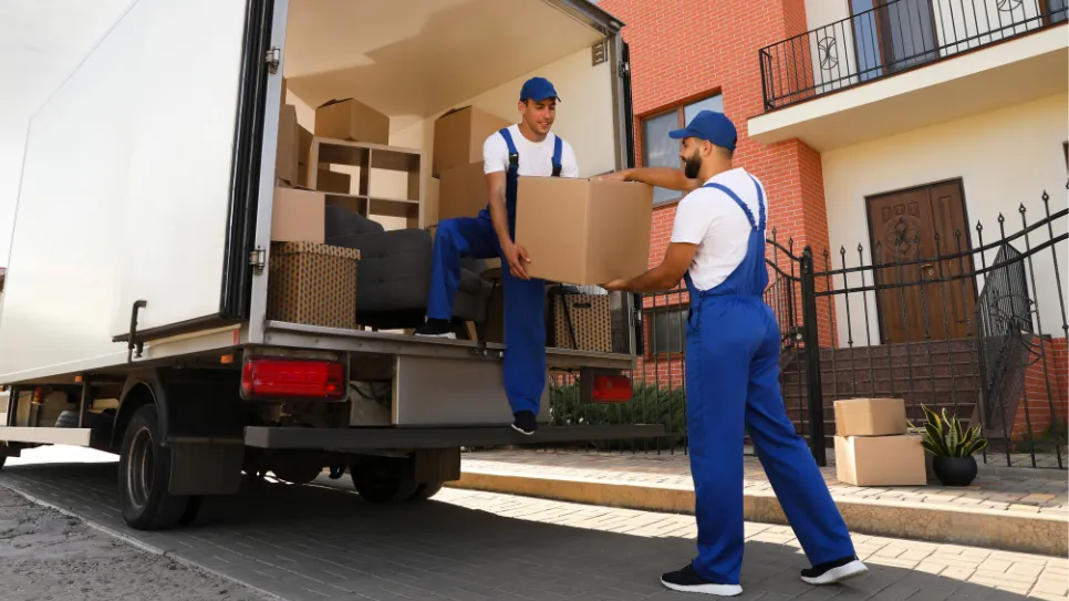 Delavca prenašata škatlo s tovornjaka pred hišo.