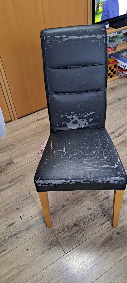 A black leather chair with visible wear, peeling and cracks on the seat and backrest surfaces.