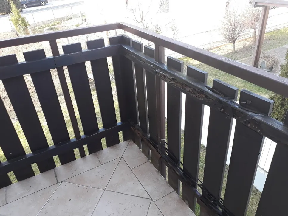 Wooden balcony railing with visible damage and decay in the external corner area.