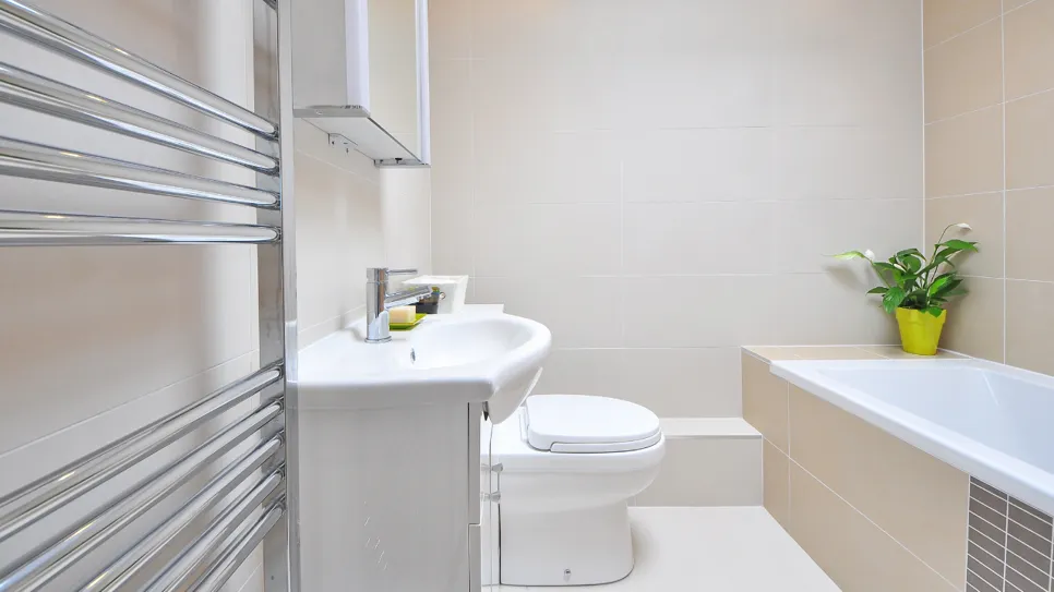 Nova kopalnica Moderna kopalnica v bež barvi z belo sanitarno opremo in kovinskim radiatorjem.