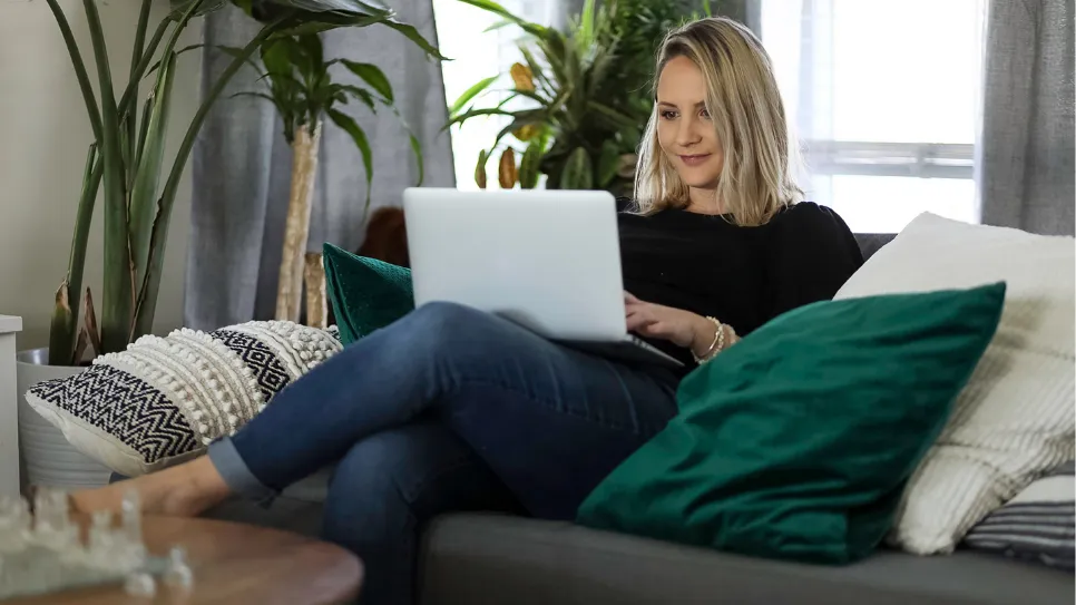 Samostojna podjetnica na kavču gleda v prenosnik.