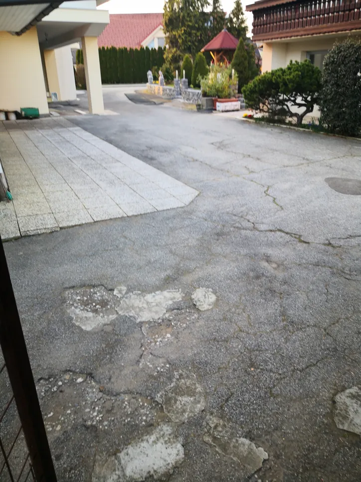 Concrete driveway with visible cracks and surface damage, requiring attention and possible repair.