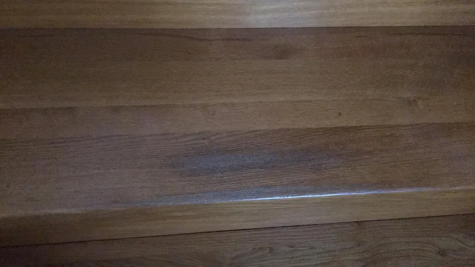 Smooth, brown wooden staircase tread with visible wear and fading in the middle.