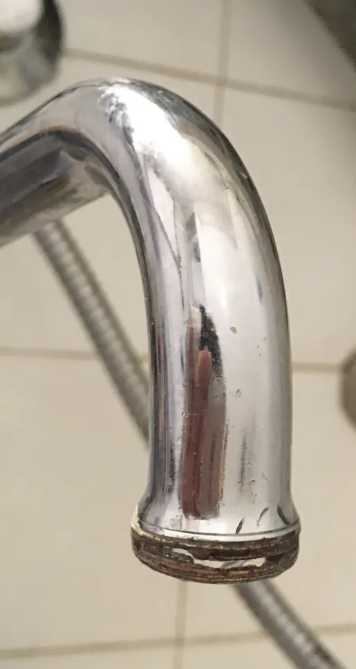 Close-up of a chrome faucet with noticeable mineral buildup around the spout in a tiled bathroom.