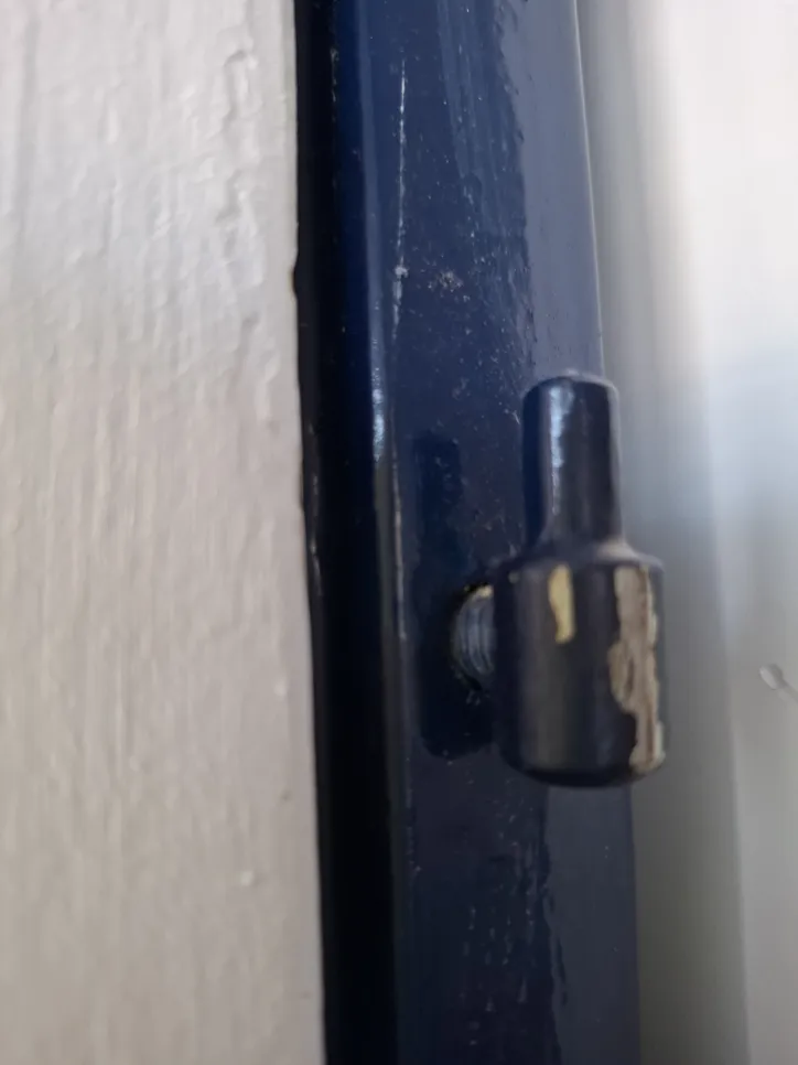 Pogled od blizu na nepravilno poravnani zatič tečaja na pobarvanem okvirju vrat.