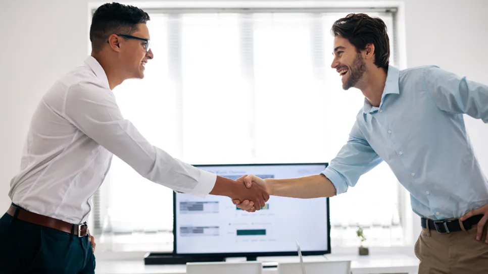 računovodja in stranka sta si podala roke pred računalniškim monitorjem, na katerem je program za spletno računovodstvo