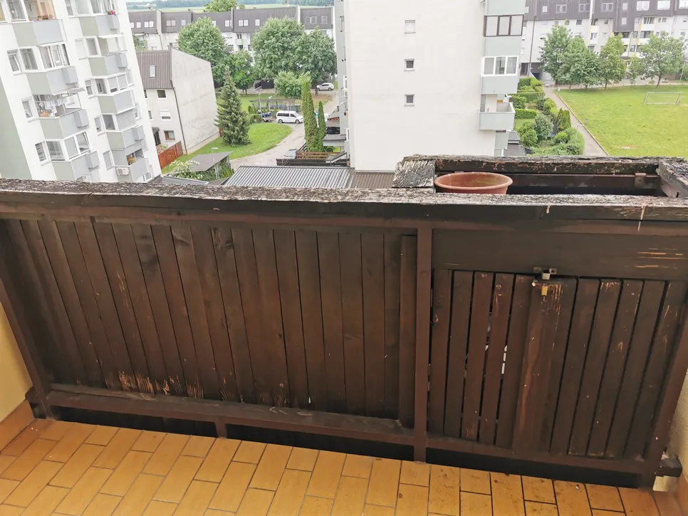 Worn and damaged wooden balcony railing with visible peeling paint and decay.