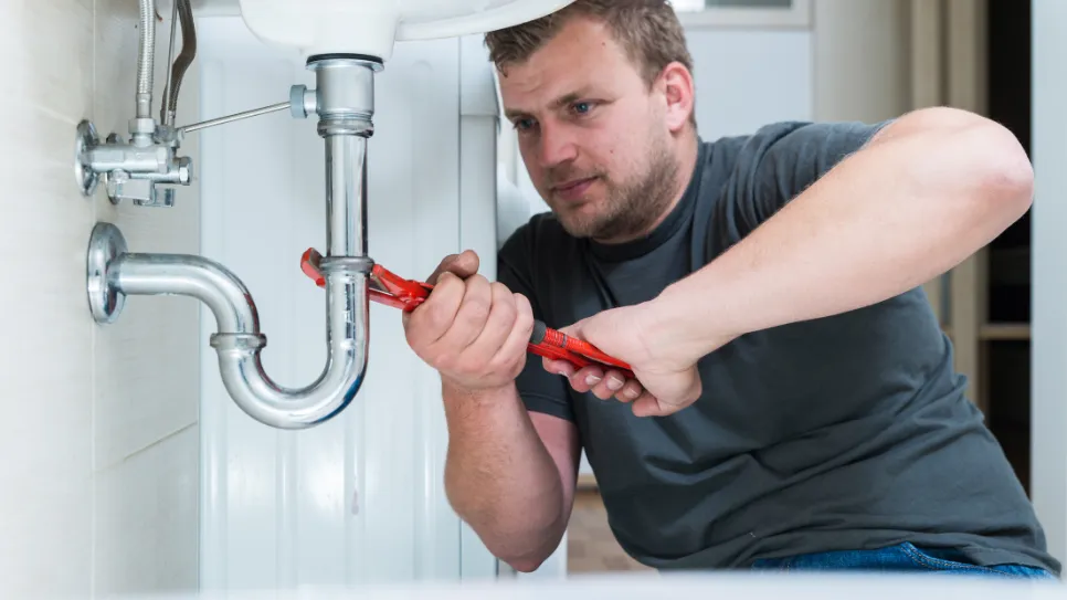 Vodovodar odteguje tesnilo na cevi pod umivalnikom.