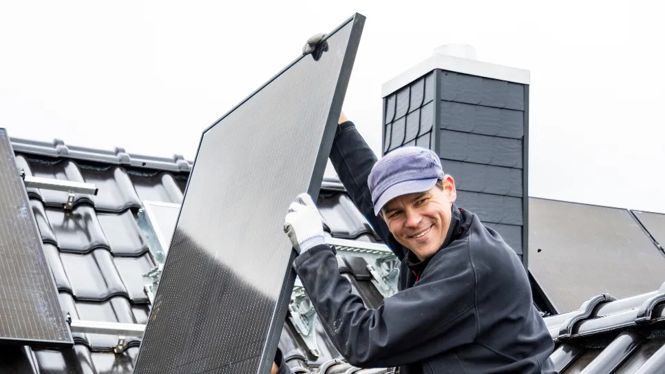Monter sončnih elektrarn na strehi s panelom v roki se zadovoljno smehlja, ker je dobitnik Primerjam.si Top 50 nagrade.