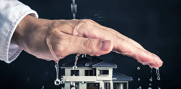 Roka varuje model lesene hiške pred vodo.