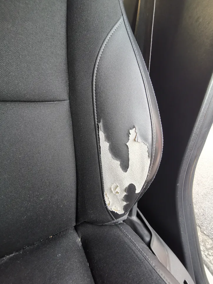 Worn fabric on a black car seat shows visible tears and damage, indicating need for upholstery repair.