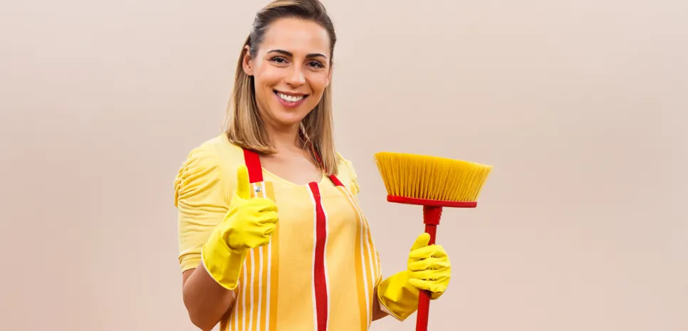 Mlada čistilka z metlo drži v zrak iztegnjen palec.