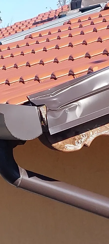 Bent metal roof gutter causing potential water drainage issues on tiled roof.
