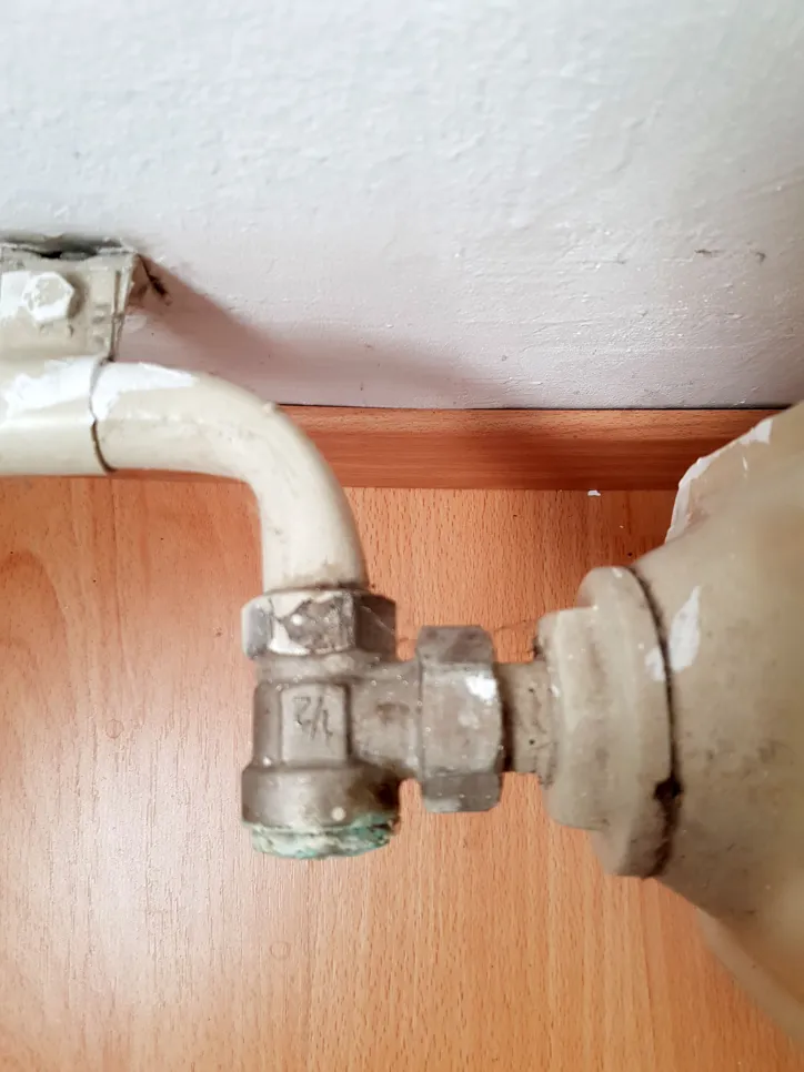 Corroded radiator valve indicating potential coolant leakage causing water stains on wooden floor.