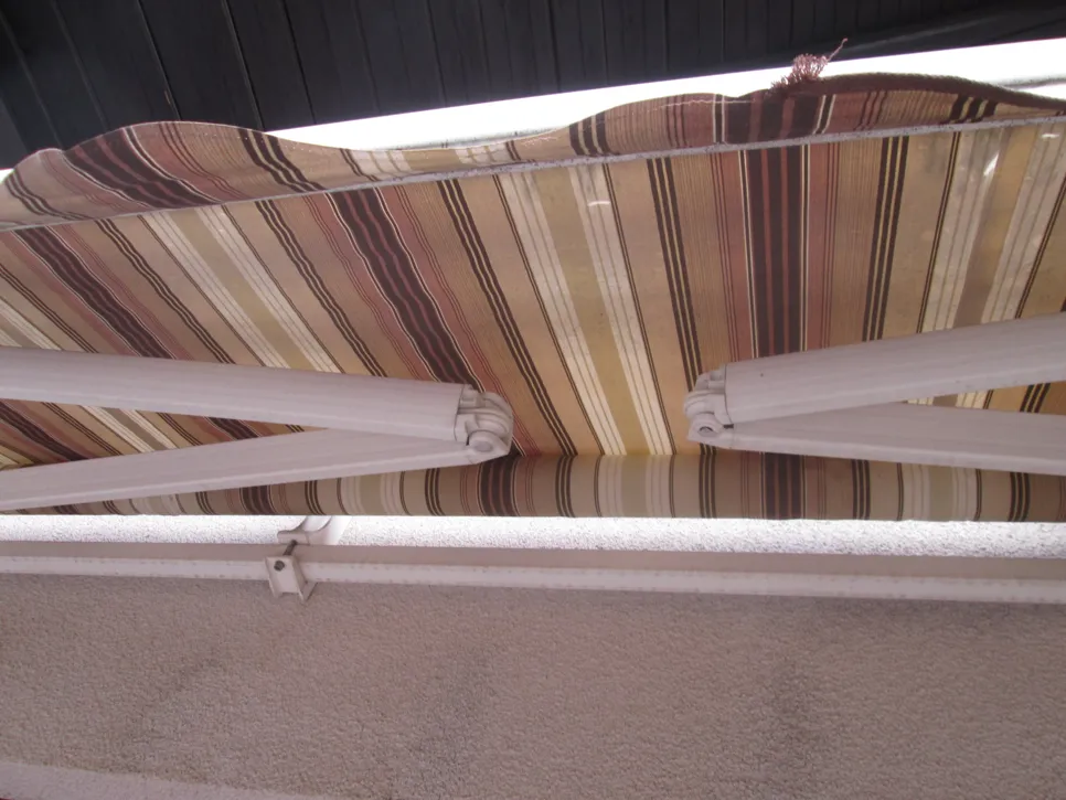 Close-up of a striped fabric retractable awning mechanism attached to a wall, highlighting joint and fabric details.